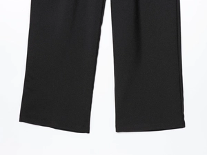 Detail of wide leg trousers hem showing black woven twill fabric texture and fine stitching