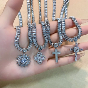 Silver iced-out cross and clover pendants on necklaces worn on hand, elegant jewelry set