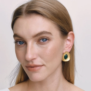 Close-up of a model wearing retro gold earrings with green resin insets and irregular shape