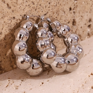 Macro view of silver hollow cloud bead hoop earrings on a textured stone surface