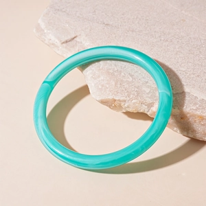 Close-up of mint green acrylic bangle with marble texture on a natural stone surface