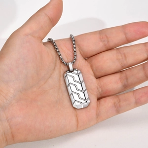 Macro detail of men's stainless steel pendant showing geometric tire pattern and box chain