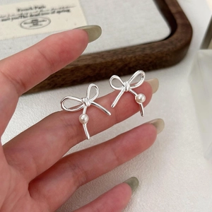 Minimalist 925 sterling silver bow knot pearl stud earrings held by hand for scale