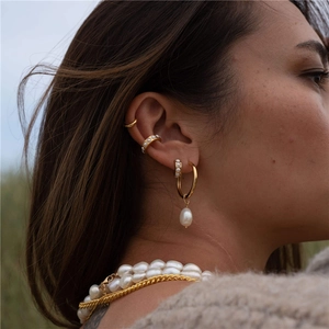 Detail of elegant gold pearl earrings and ear cuff set worn by a female model