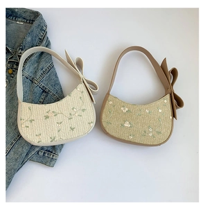 Detail of floral embroidery and large bow on straw-textured crossbody bag with PU trim