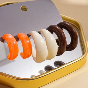 Nahaufnahme eines 3er-Sets C-förmiger Acryl-Ohrringe in Orange, Beige und Dunkelbraun