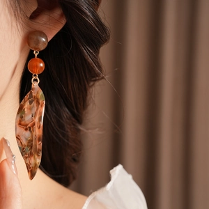 Close-up of dangling acetate leaf earring with brown beads and green mottled texture