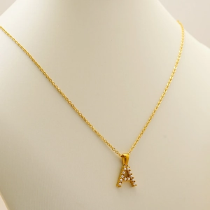 Close-up of gold-plated necklace featuring a pearl-inlaid letter A pendant on a mannequin