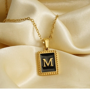 Detailed close-up of a square 18K gold letter M pendant on luxury gold silk background