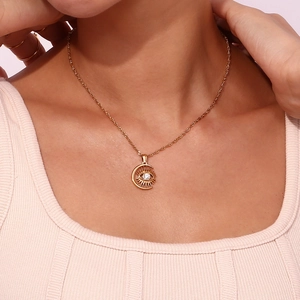 Close-up of gold twist chain necklace with sun eye and moon pendant worn by model
