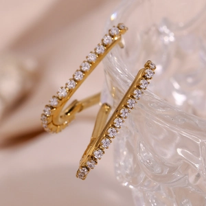 Close-up of gold-plated U-shaped earrings with white zircon inlay on glass edge