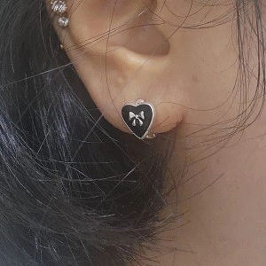 On-ear view of minimalist black heart earrings featuring a silver bow tie accent
