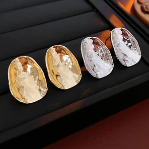 Detailed view of irregular hammered metal stud earrings in gold and silver finish