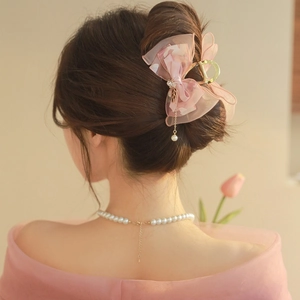 Elegant pink tulle bow hair claw clip with gold accents and a pearl pendant on a model