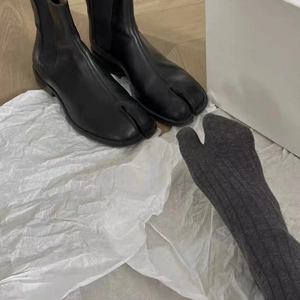 Detail of grey Tabi split-toe socks paired with black leather Tabi boots on white paper