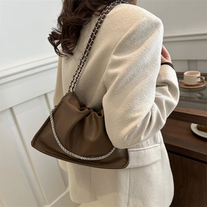 Brown ruched leather underarm bag with silver chain strap shown in a cafe setting