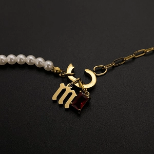 Close-up of gold letter M pendant and red gemstone on a pearl and chain necklace.