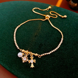Détail d'un bracelet croix doré avec perles et breloques en forme d'étoile sur velours