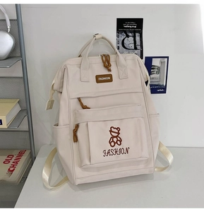 Detail view of cream canvas backpack with front zipper pocket in a student workspace setting