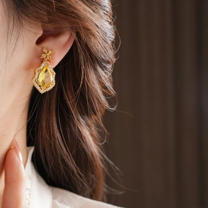 Close-up of model wearing gold drop earrings with pear-shaped yellow stone and diamonds