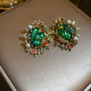 Close-up of Baroque emerald earrings with gold filigree, pearls and enamel details