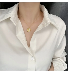 Detailed shot of a gold butterfly shell pendant on a fine chain worn with a white shirt