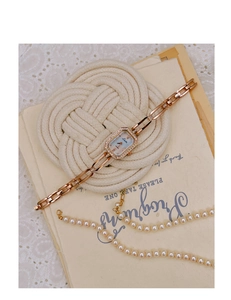 Detailed close-up of rose gold rectangular watch with crystal bezel and chain strap