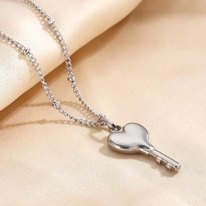Detailed view of silver heart key pendant on a beaded chain over silk fabric
