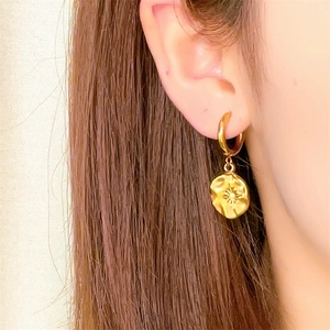 Gros plan d'un mannequin portant des boucles d'oreilles rondes dorées avec gravure