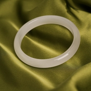 Close-up of a white cat eye stone bangle on elegant olive green silk fabric