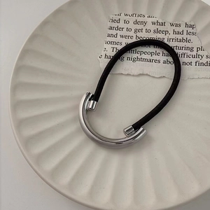 Detail of minimalist black elastic hair tie with a polished silver metal curved charm