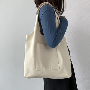 Detail of minimalist beige canvas tote bag with large front pocket and wide shoulder strap
