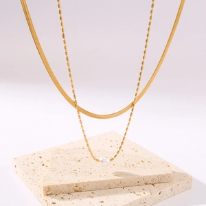 Double-layered 18K gold plated snake chain necklace with pearl pendant on stone background