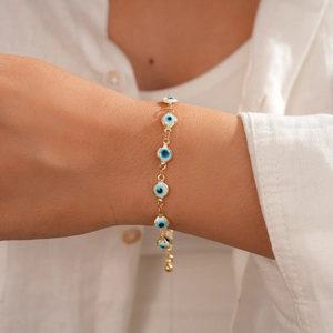 Gros plan d'un bracelet en chaîne dorée avec des breloques œil bleu en émail au poignet
