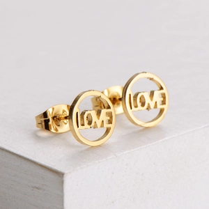 Titanium steel LOVE hollow stud earrings with 18k gold plating on a white platform