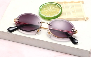 Detail of rimless oval sunglasses with purple gradient lenses and gold metal temples
