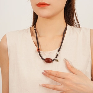 Detail of red agate pendant necklace with woven cord worn on a model in beige top