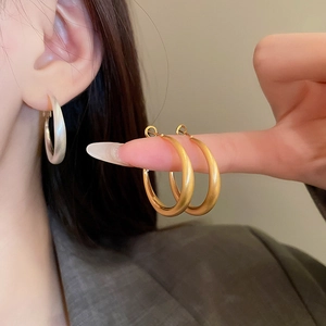 Close-up of matte brushed metal hoop earrings in gold and silver finish on a model
