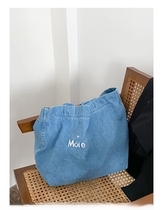 Sac fourre-tout en denim bleu avec broderie Less Mondays More Sundays sur une chaise