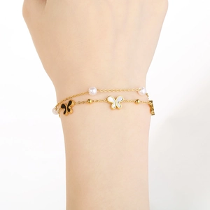 Detail of gold double-layer bracelet featuring pearl accents and butterfly charms on wrist