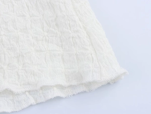 Macro view of white textured seersucker fabric with frayed edge detail on women's skirt