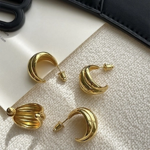 Close-up of golden C-shaped hoop earrings with triple-layered textured metallic stripes