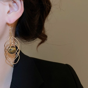 Close-up of dangling golden rhombus frame earrings with brown tiger eye stone on model