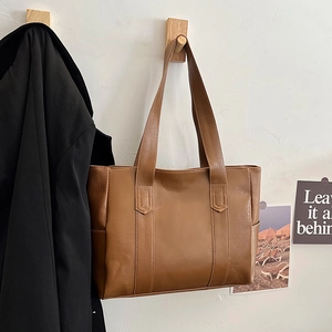 Brown leather tote bag with double straps hanging on a wall hook in a minimalist setting