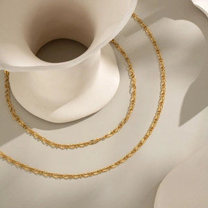 Minimalist 18K gold stainless steel chain necklace draped on a white ceramic vase