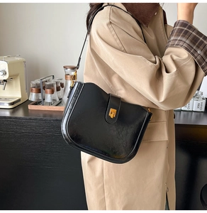 Detail of vintage black saddle bag with gold rotating lock on a classic trench coat