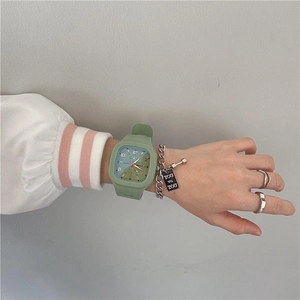 Close-up of green square digital watch and silver chain bracelet with 'YOU VS YOU' tag