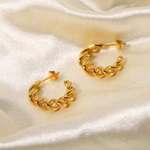Macro shot of 18K gold-plated twisted rope C-hoop earrings on cream silk fabric