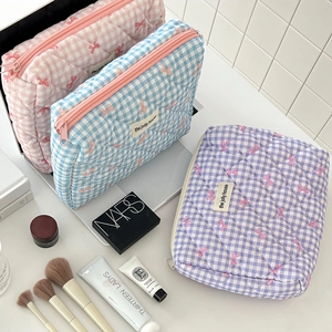 Three quilted checkered makeup bags with bows organized with beauty accessories on a desk