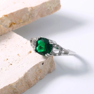 Macro detail of silver ring with emerald gemstone and pavé zircon on stone slab